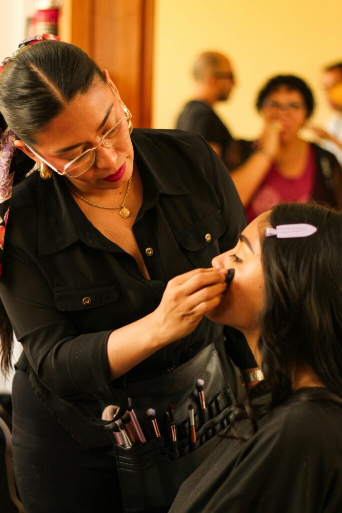 A makeup artist applies cosmetics to a model in a busy studio setting.