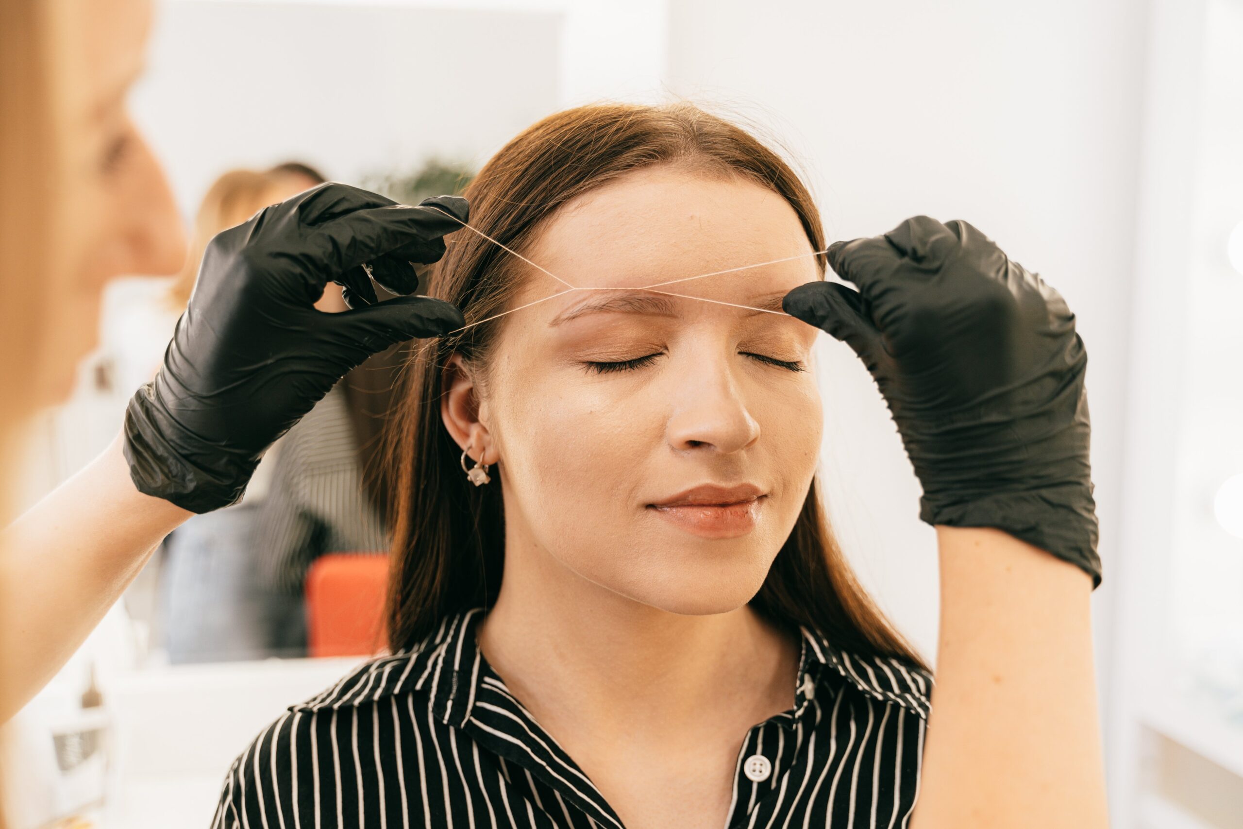 A woman receives precise eyebrow threading in a modern salon setting.